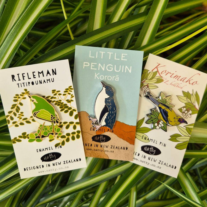 Three enamel pin cards with bird illustrations on a grass background