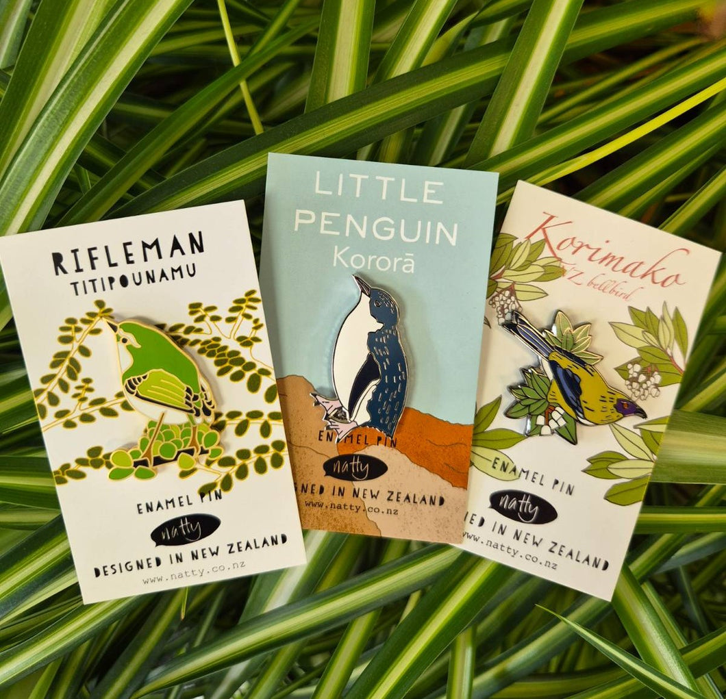 Three enamel pin cards with bird illustrations on a grass background
