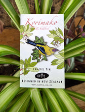 Enamel pin packaging with a Korimako bird design on a white background, surrounded by green leaves.